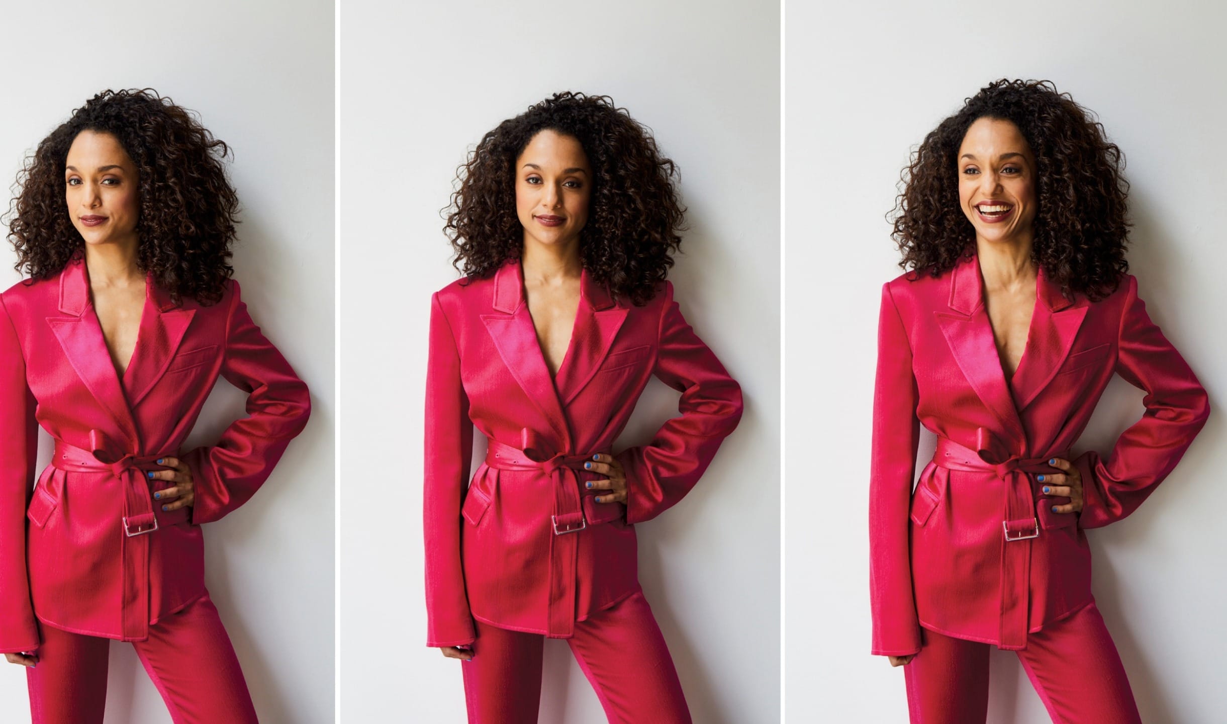 A person with curly hair modeling a vibrant red blazer and pants, posing confidently against a white background.
