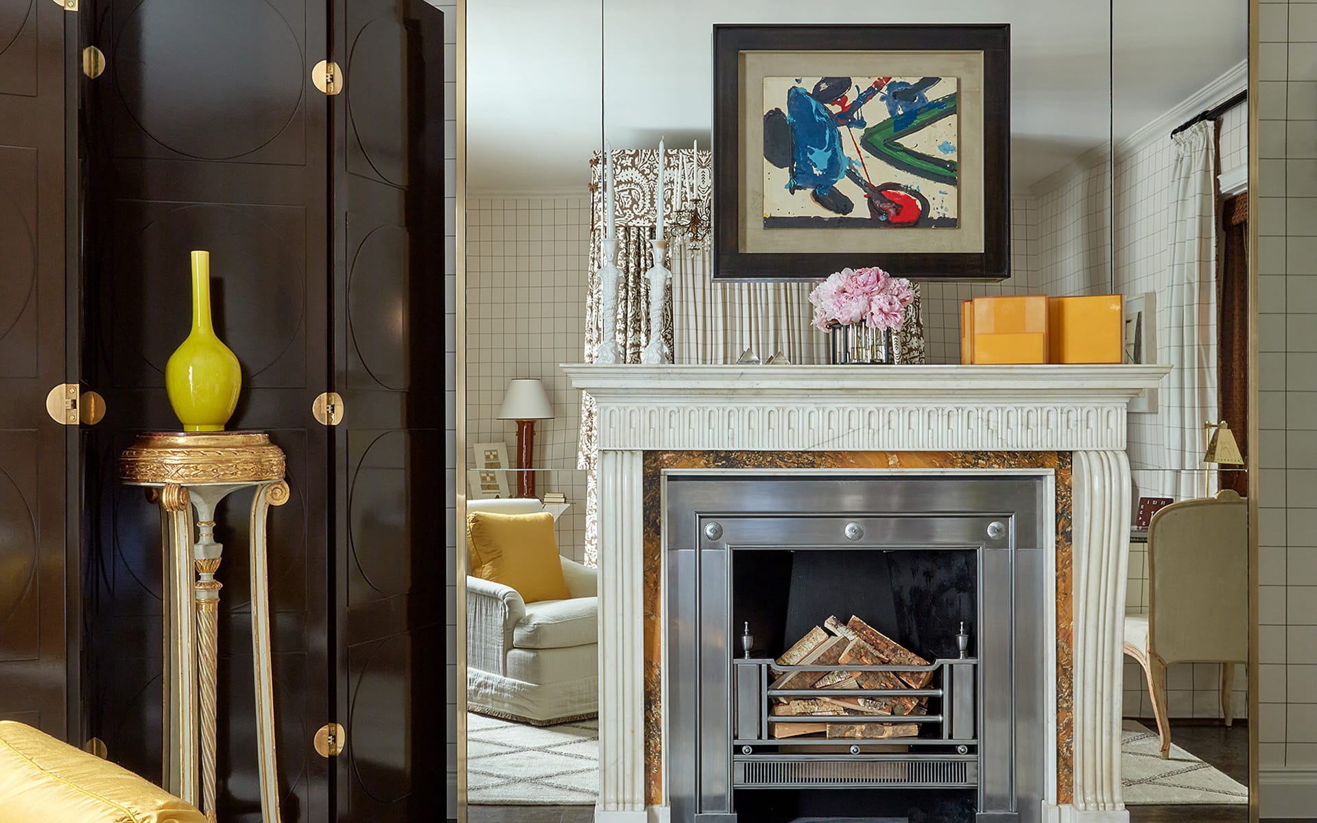 Elegant living room with ornate fireplace, abstract painting, yellow vase on stand, and plush seating in a classic setting.