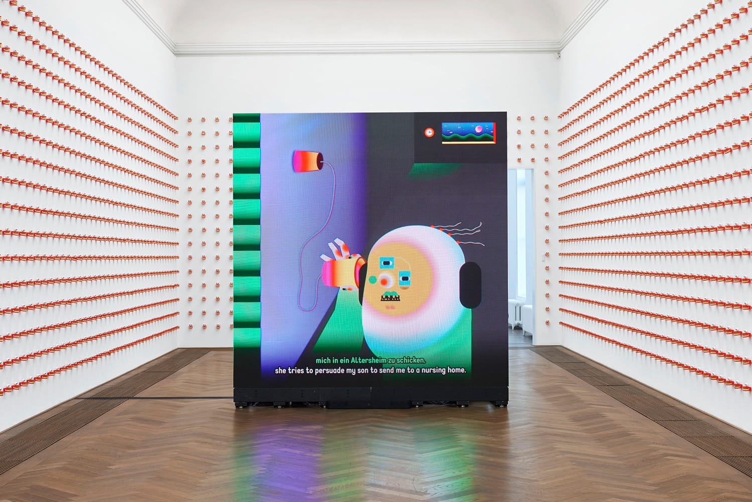 Digital artwork in a gallery with colorful abstract shapes displayed on a large screen, surrounded by objects on the walls.