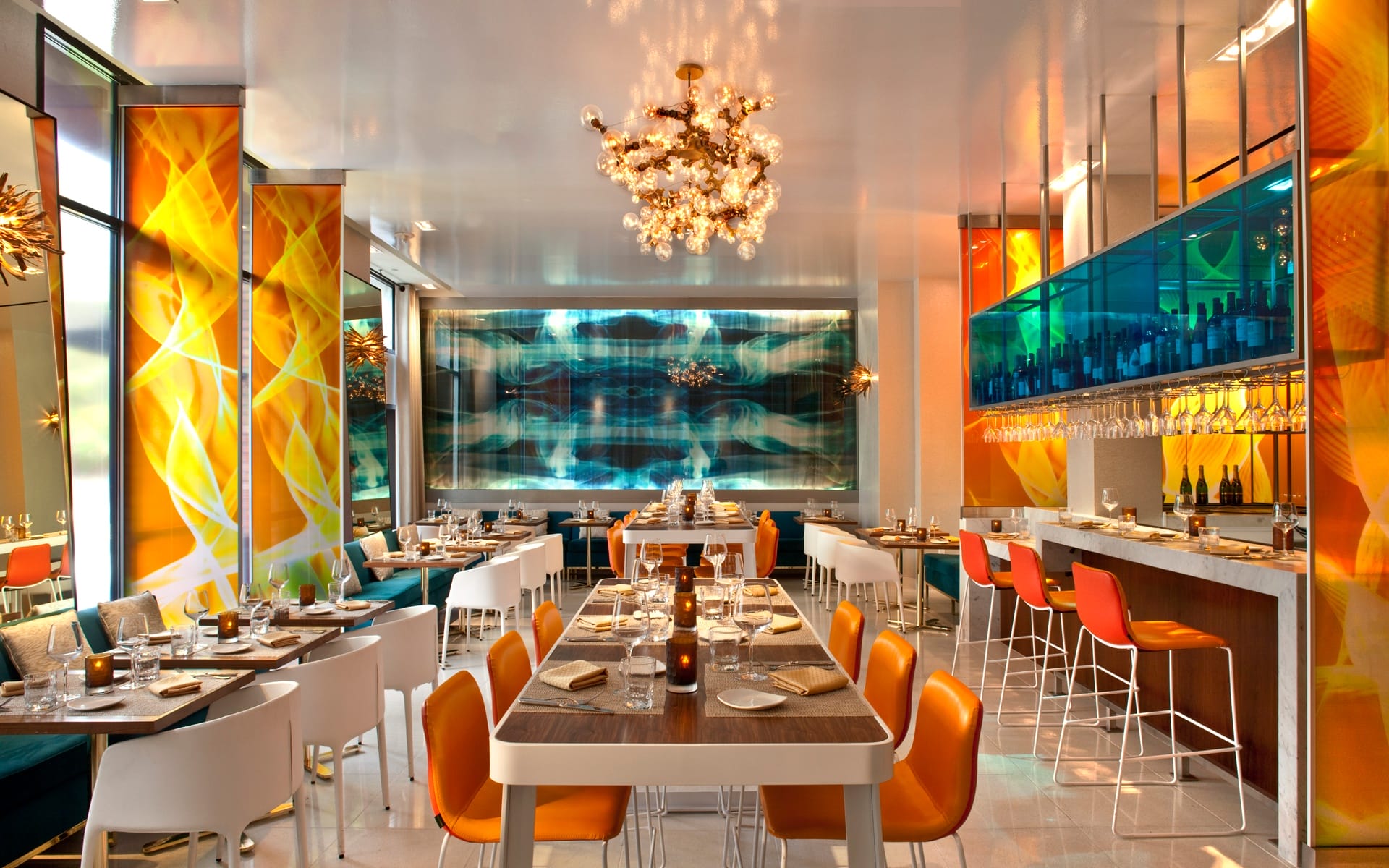Modern restaurant interior with colorful decor, elegant chandeliers, and neatly arranged tables and chairs.