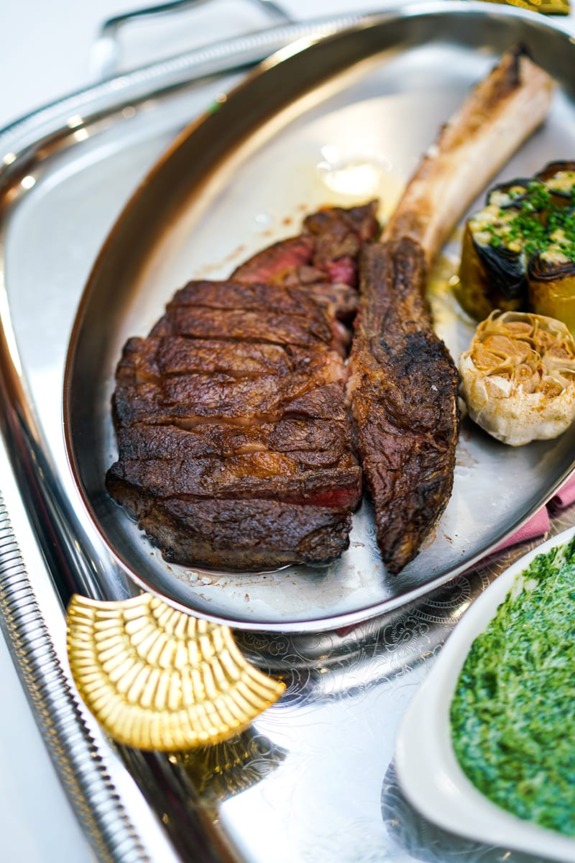 Grilled tomahawk steak served with roasted garlic and creamy spinach on a silver platter.