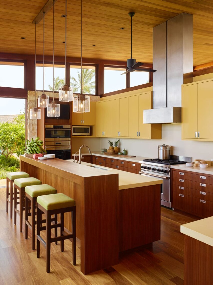 Modern kitchen with wood accents, yellow cabinetry, and pendant lighting, featuring a central island with green stool seating.