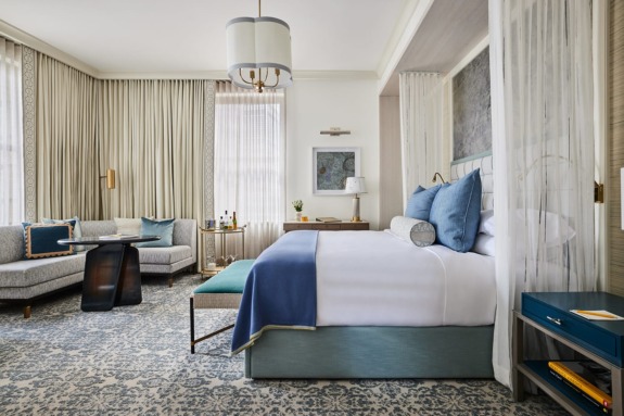 Luxurious hotel bedroom with a large bed, elegant sofa, and stylish decor in soothing blue and cream tones.