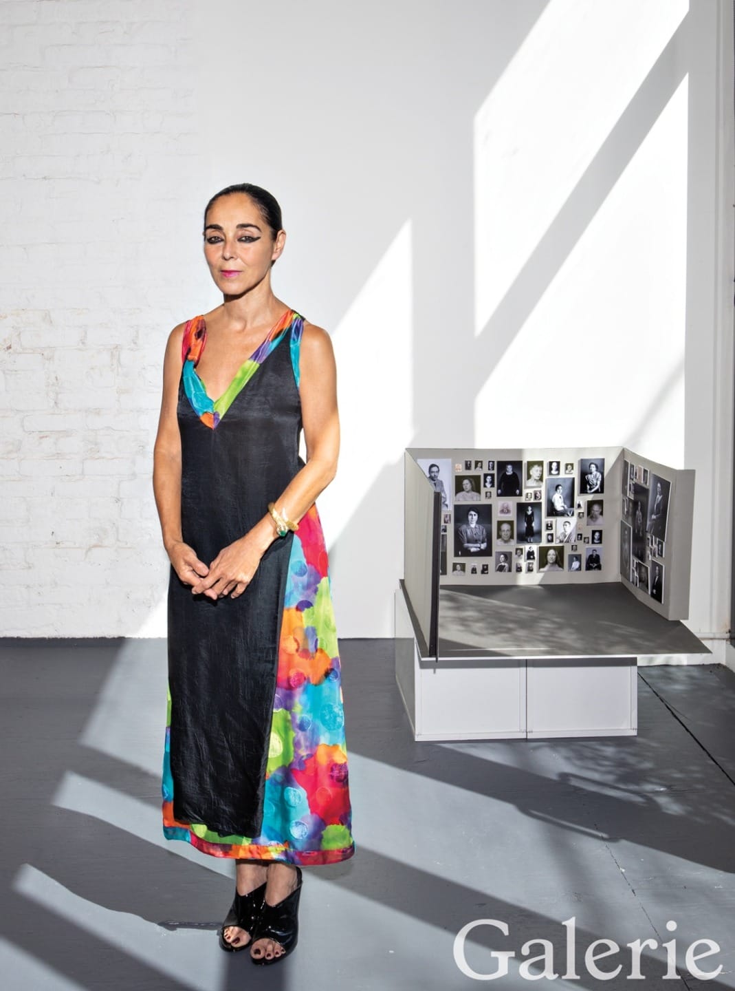 Person in colorful dress standing by art display with photographs in a gallery setting.