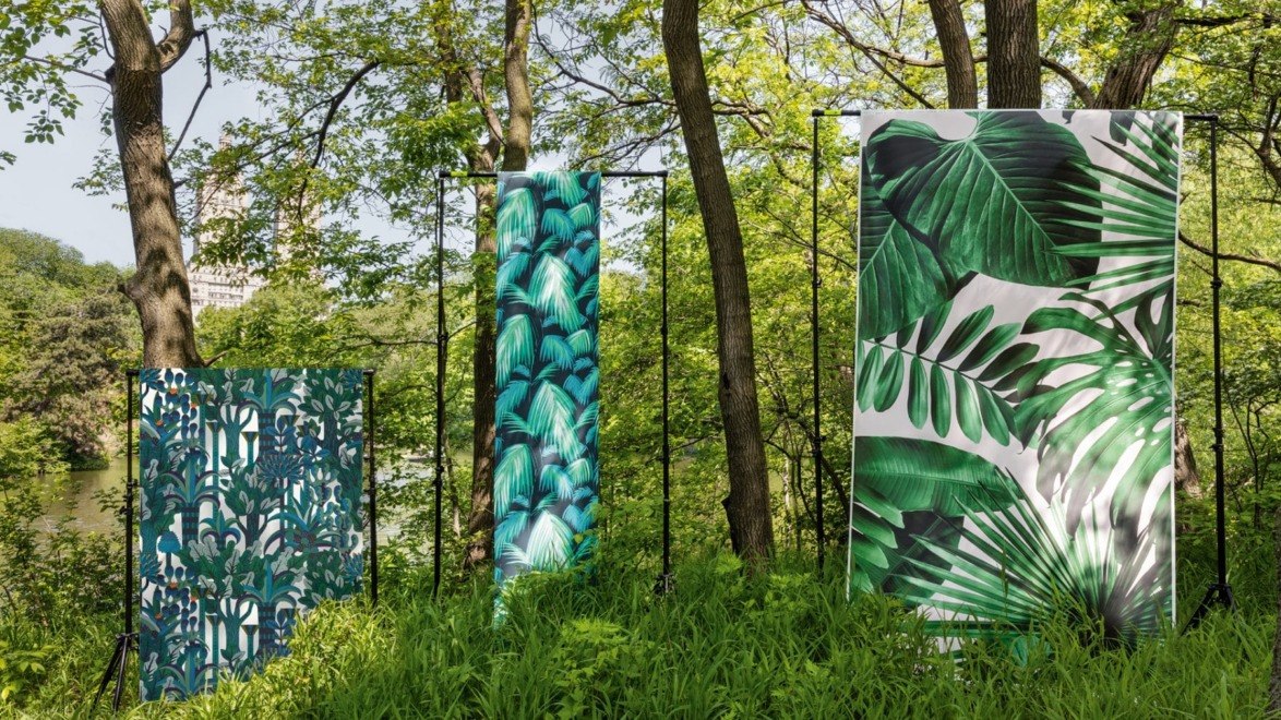 Three large panels with green leafy patterns stand amidst lush greenery and trees in a park setting.