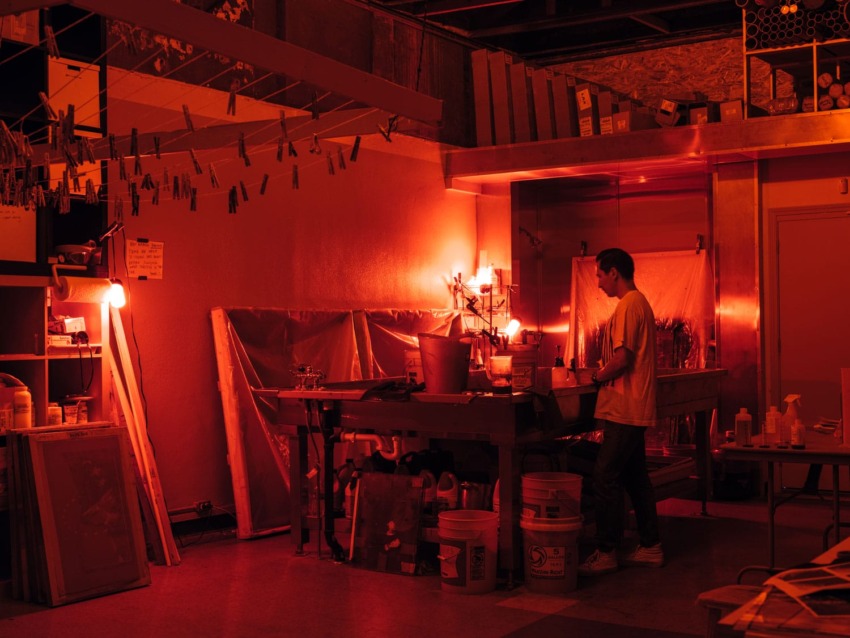 Person working in a red-lit darkroom with various supplies around, creating an atmospheric and focused scene.