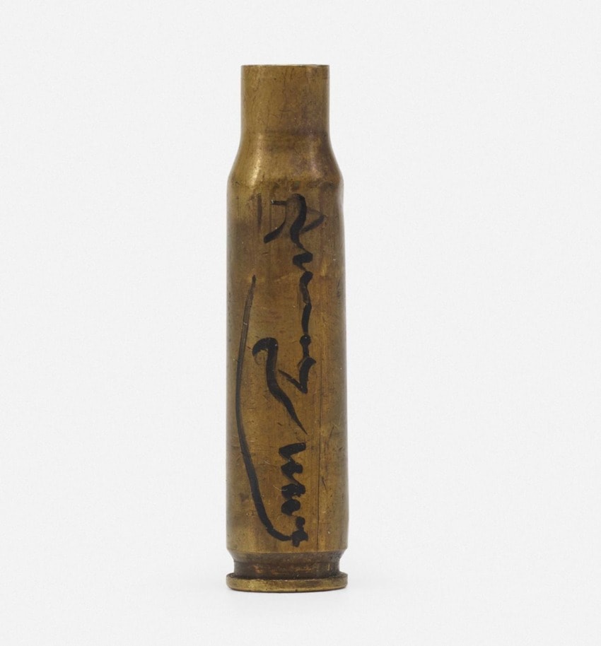 Brass bullet casing with handwritten markings on a white background