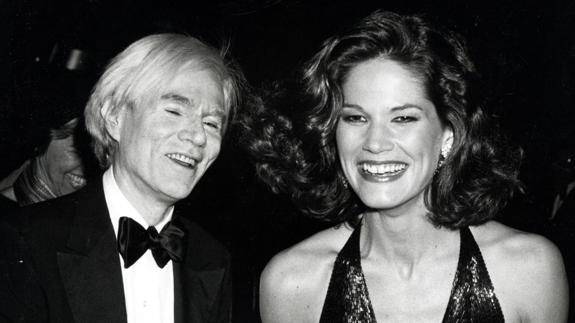 A man in a tuxedo and a woman in a sequin dress smiling at a glamorous event.