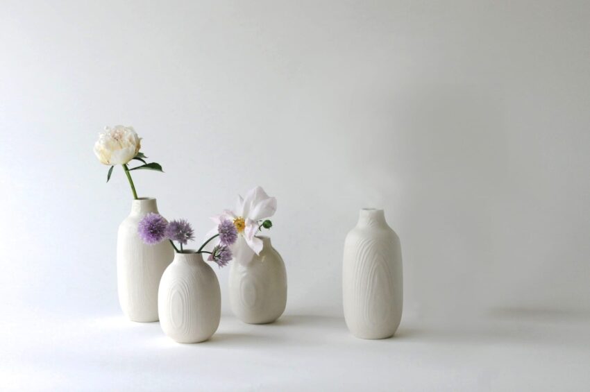 Four white ceramic vases with flowers against a plain background.