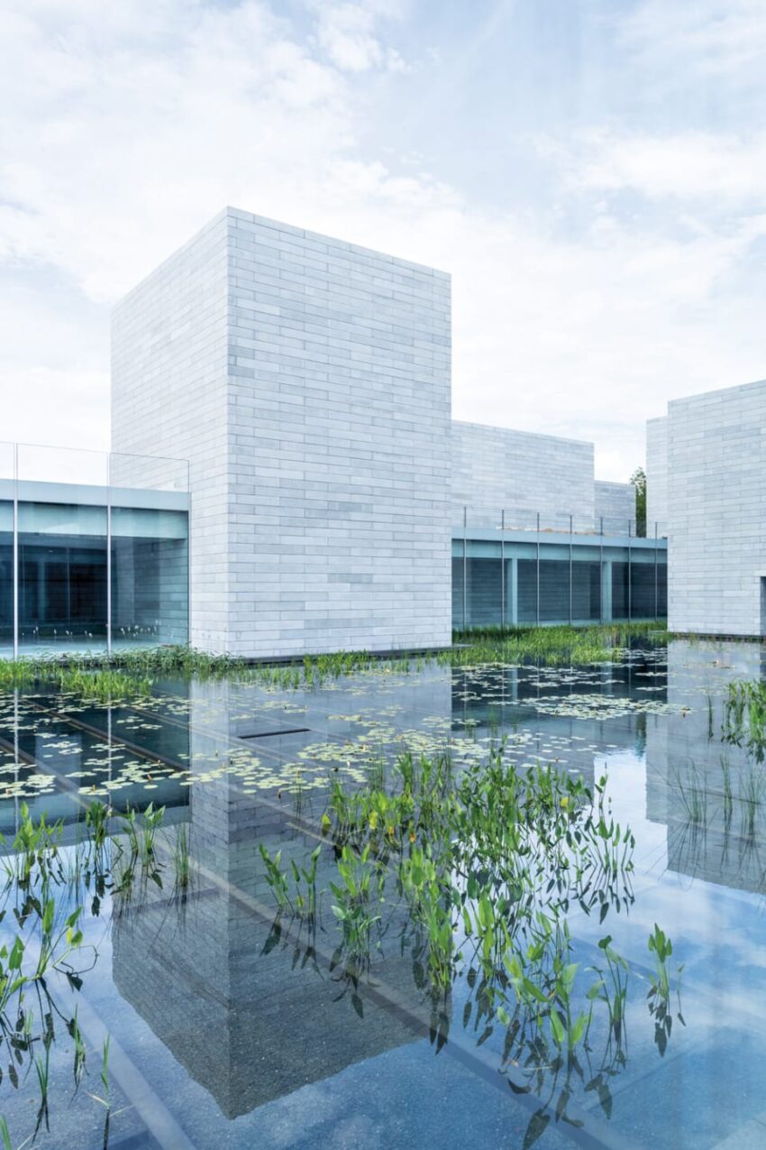 Modern architecture with reflective water garden and sky backdrop.