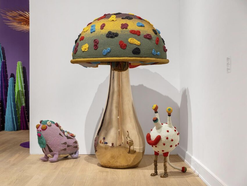 Colorful, whimsical mushroom sculpture with two quirky, plush creatures in an art gallery setting.
