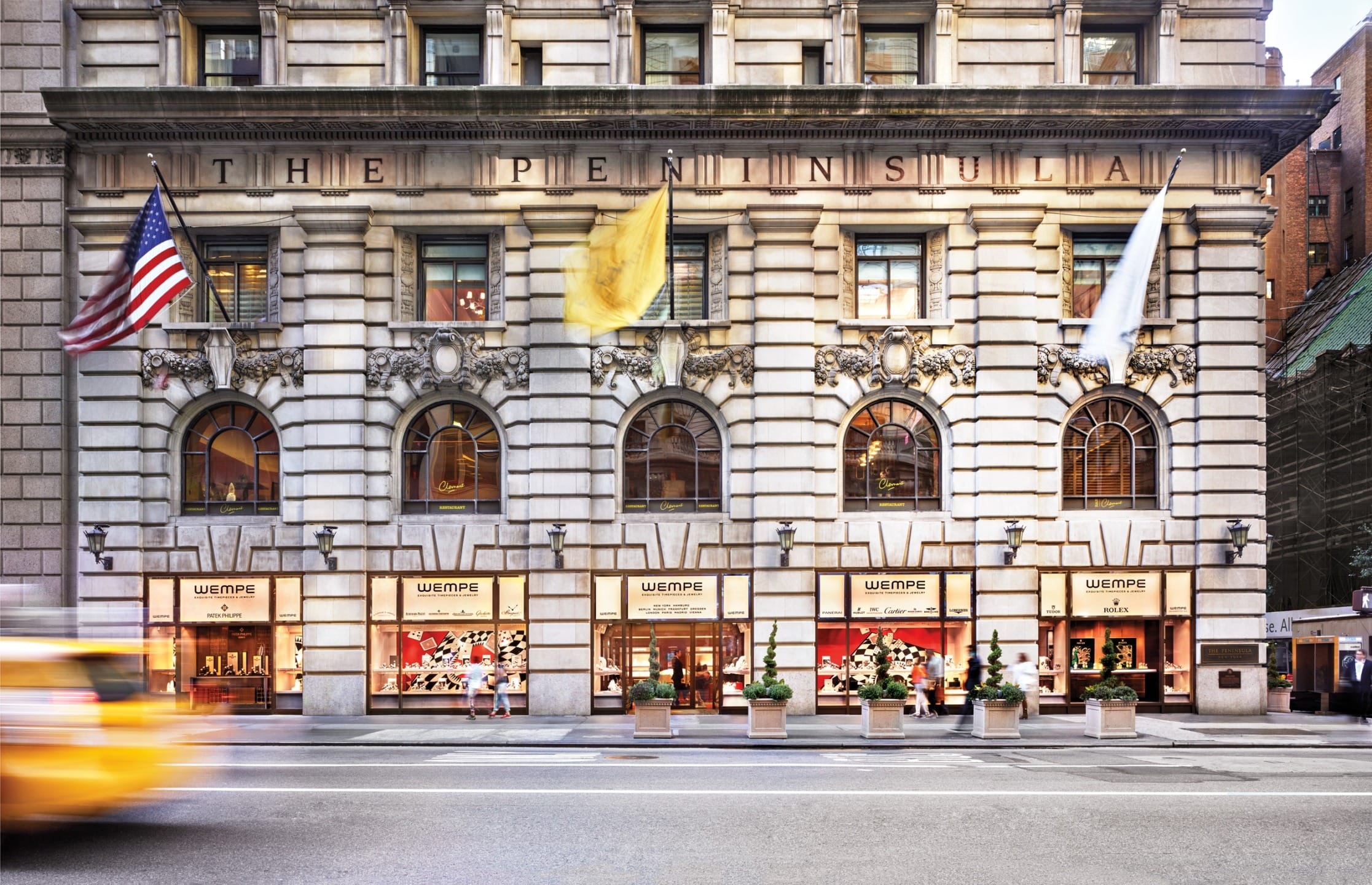Historic building exterior with flags and large windows displaying Christmas decorations, blurred taxi passing in foreground.