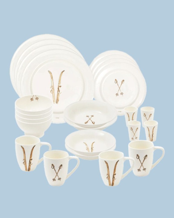 A set of white ceramic dinnerware with gold ski-themed designs against a light blue background.
