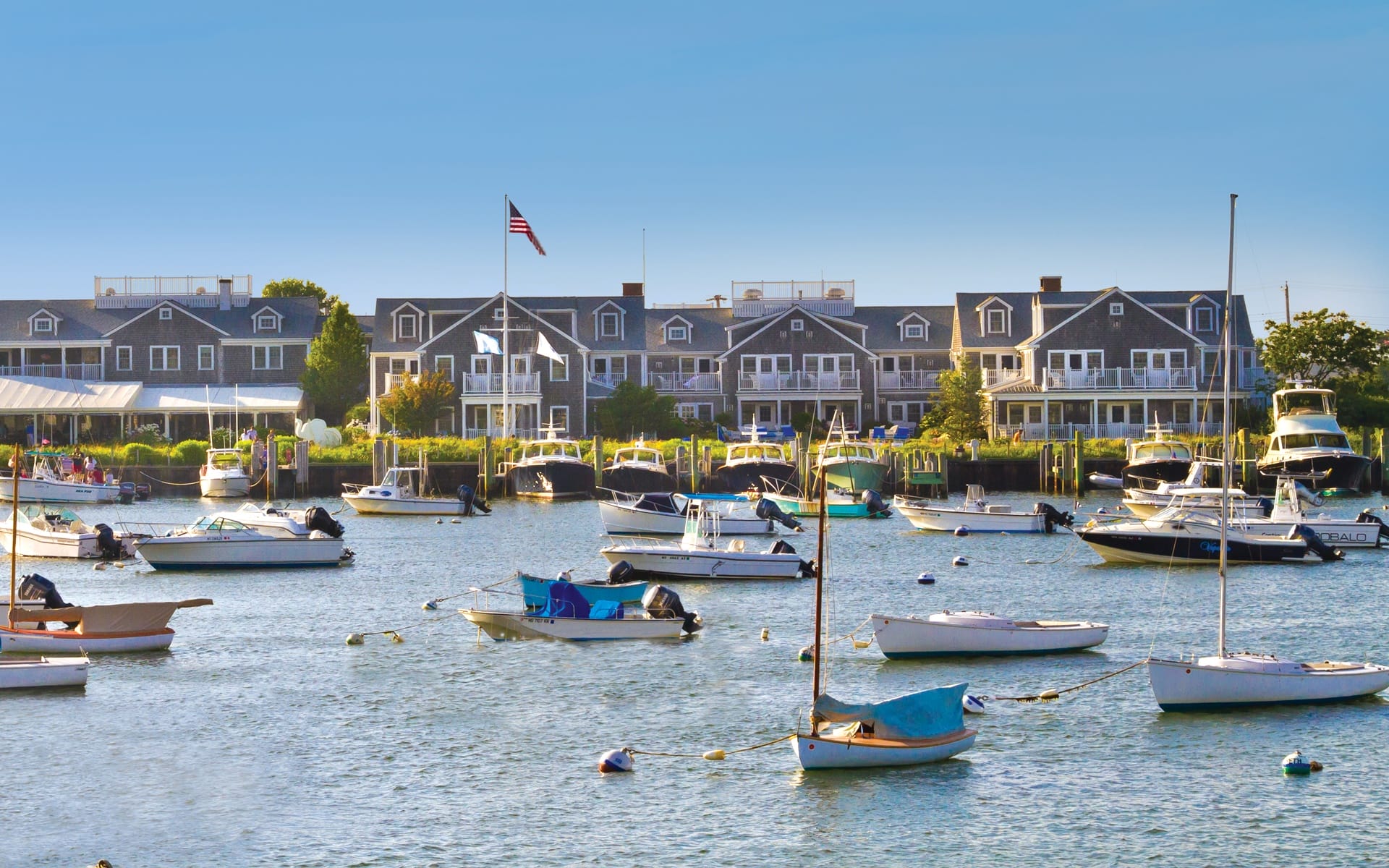 Boats moored in a scenic harbor with a backdrop of classic coastal buildings on a sunny day.