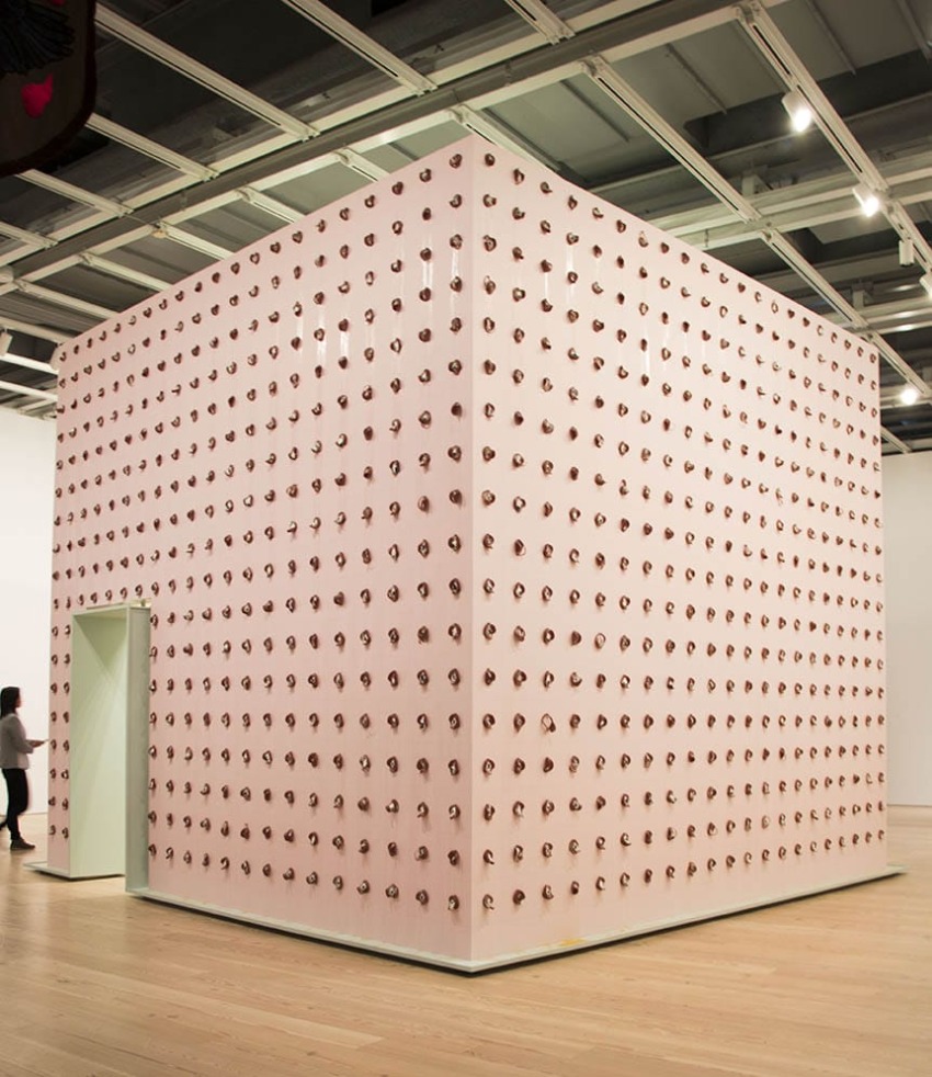 Art installation featuring a large cube covered with multiple round knobs in a gallery space with a person standing nearby.