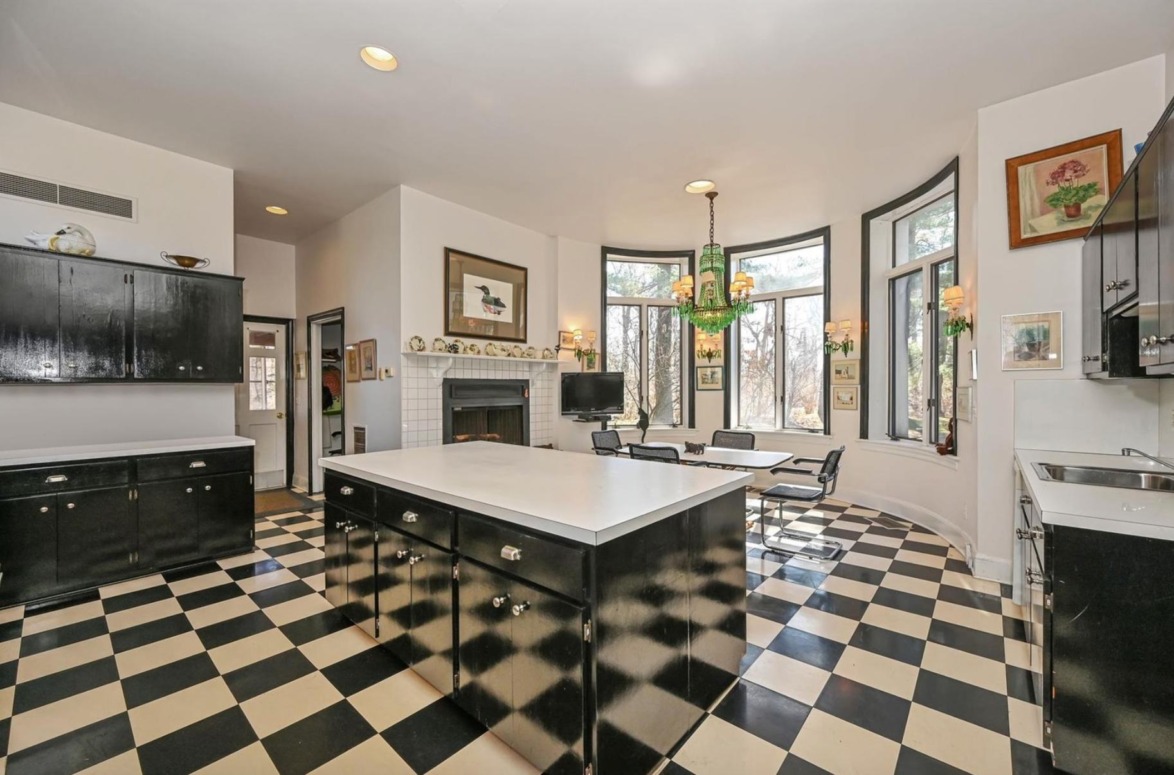 Spacious kitchen with checkered floor, black cabinets, white countertops, a fireplace, and large windows overlooking trees.