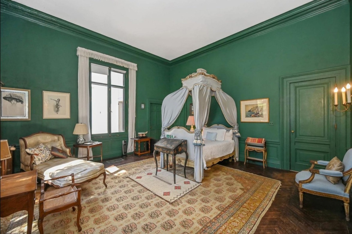Elegant vintage bedroom with green walls, canopy bed, antique furniture, framed art, and large window with white curtains.
