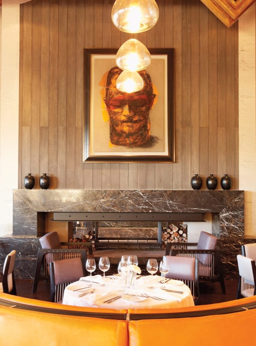 Elegant dining room with a large portrait above a marble fireplace, set table with glasses, and warm lighting.