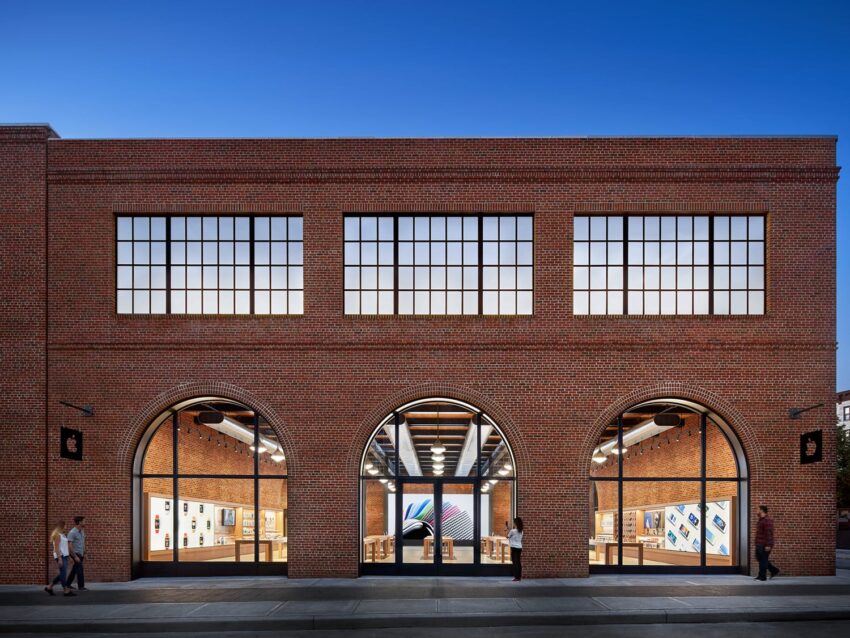 Exterior view of a brick building with arched windows and people walking in the street at dusk.