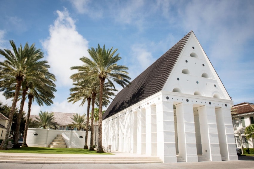 Modern white building with tall pillars and palm trees under a blue sky.