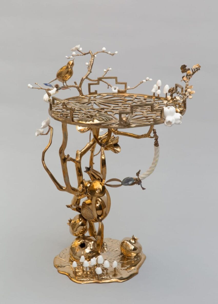 Ornate gold tree-shaped sculpture with birds, flowers, and intricate lattice design on a gray background
