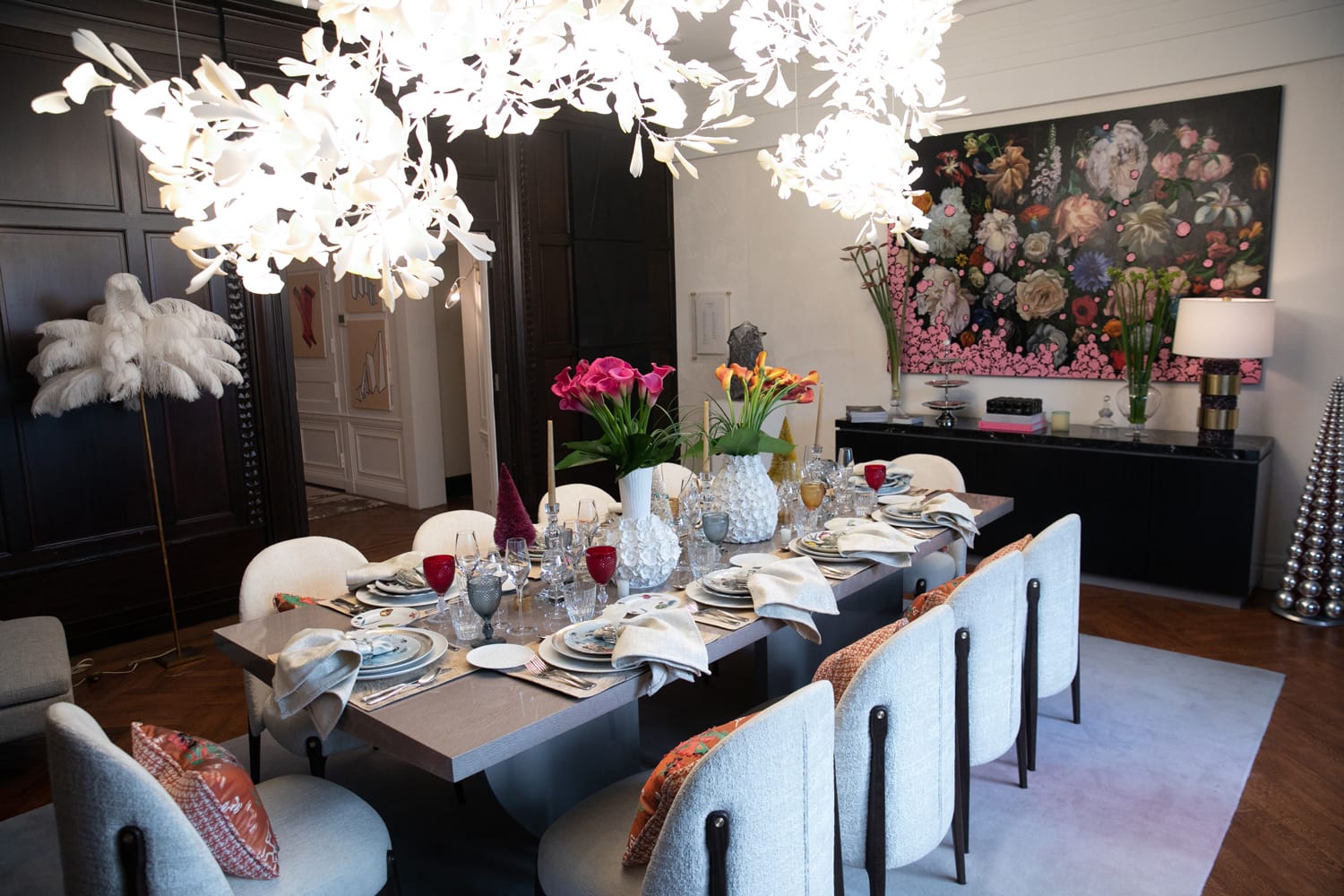 Elegant dining room with a large table set for a meal, surrounded by chairs, floral centerpieces, and decorative lighting.