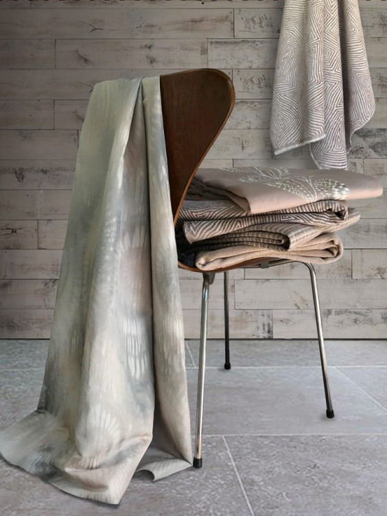 Wooden chair stacked with neutral-toned folded fabrics draped over the back against a textured wooden wall.