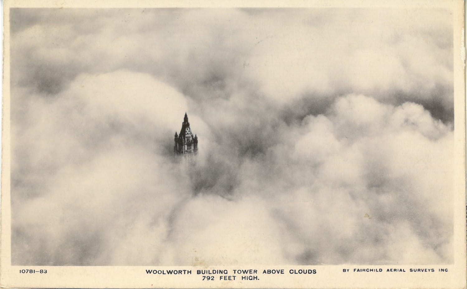 Aerial view of Woolworth Building tower peeking through thick cloud cover, measuring 792 feet in height.