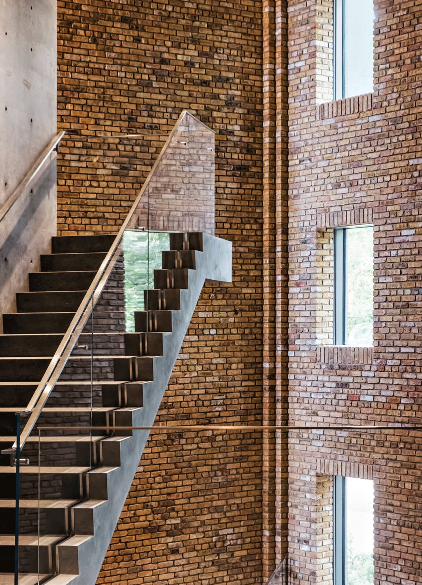 Modern staircase with glass railing and brick walls, featuring large windows that allow natural light to stream into the space.