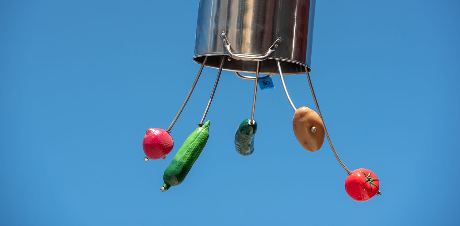 Kitchen pot with utensils holding vegetables and fruits against blue sky background.