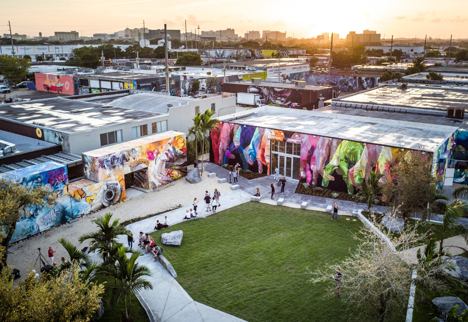 Aerial view of Wynwood Walls in Miami at sunset, showcasing vibrant murals and people enjoying the open grassy area.