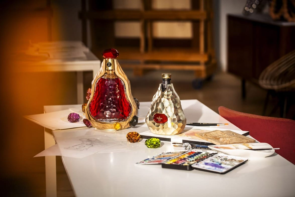Two artistic glass bottles on a table with painting supplies and colorful gems, in a creative studio environment.