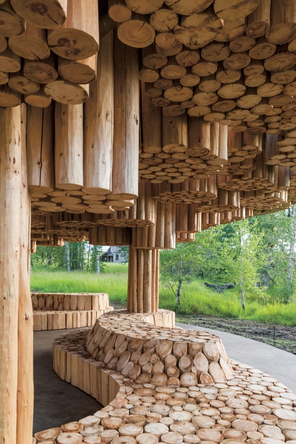 Wooden architectural structure with round timber logs, set in a green forest environment, showcasing natural design elements.