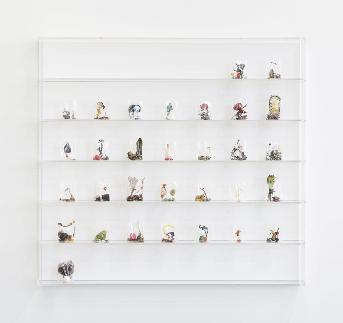 Display shelf with various small art sculptures arranged in a grid on a white wall.