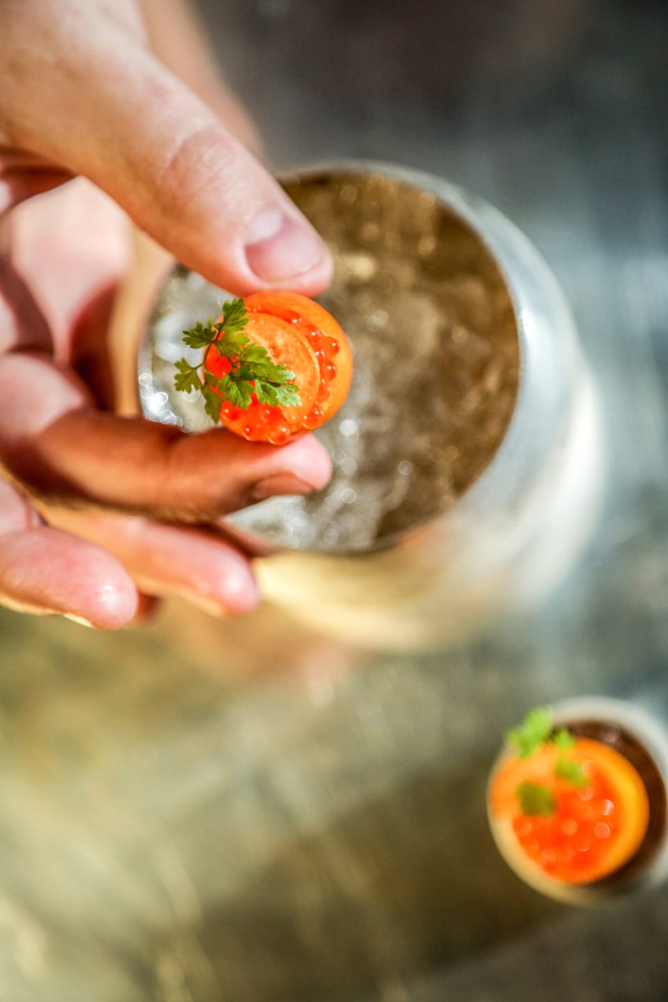 Hand holding gourmet appetizer with red caviar and fresh herb garnish, against blurred background in a culinary setting.