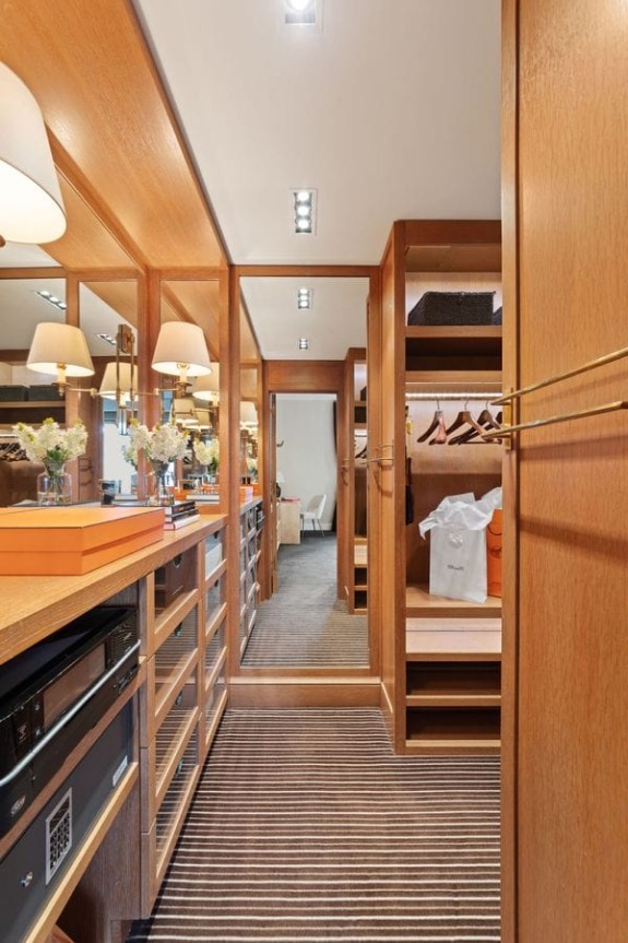 Luxurious wooden walk-in closet with mirrors, shelves, and a striped carpet floor.