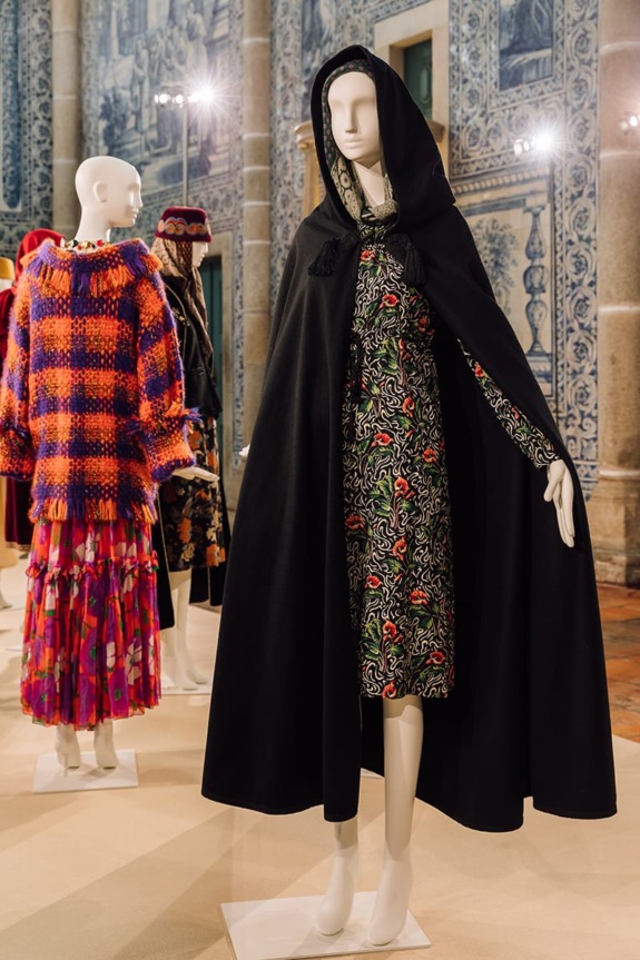 Mannequins displaying colorful, patterned clothing with hoods and capes in an artistic exhibit setting.