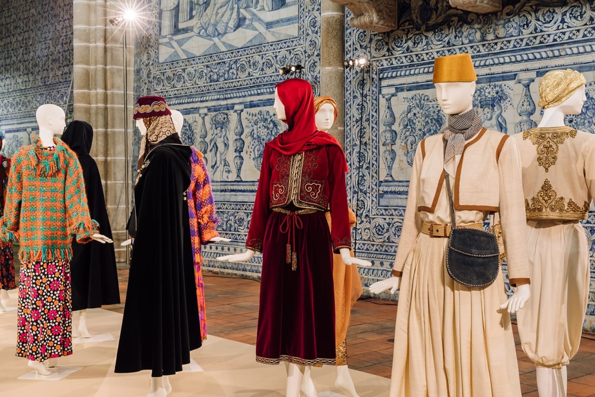 Exhibition of mannequins dressed in vibrant traditional and modern garments within a richly decorated room.