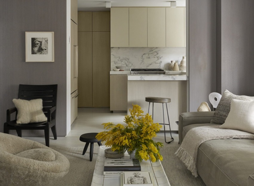 Modern living room with beige sofa, yellow flowers on table, and view of minimalist kitchen in the background.