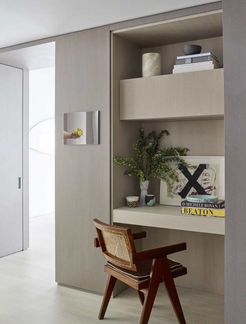 Modern home office with wooden desk, chair, and decorative shelves holding books and plants.