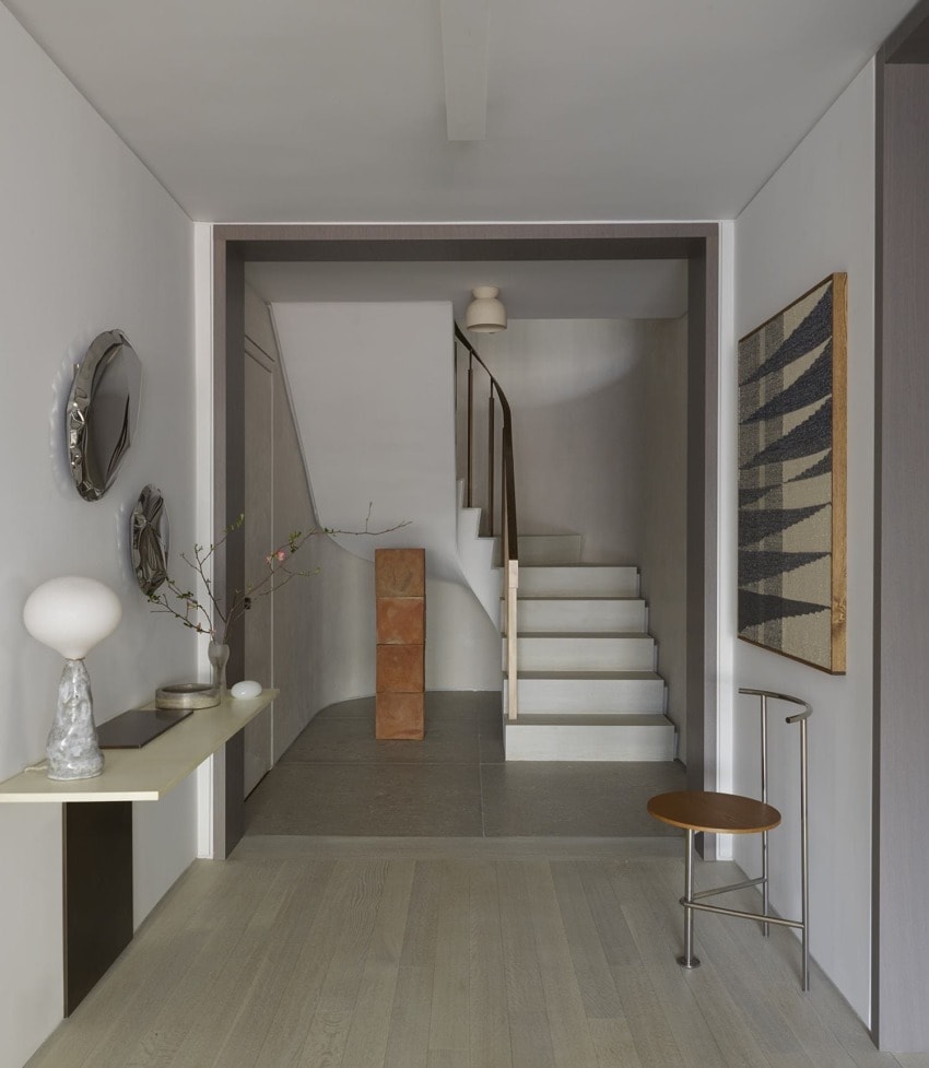 Modern hallway with a minimalist design, featuring a staircase, decorative mirrors, a side table, and contemporary artwork.