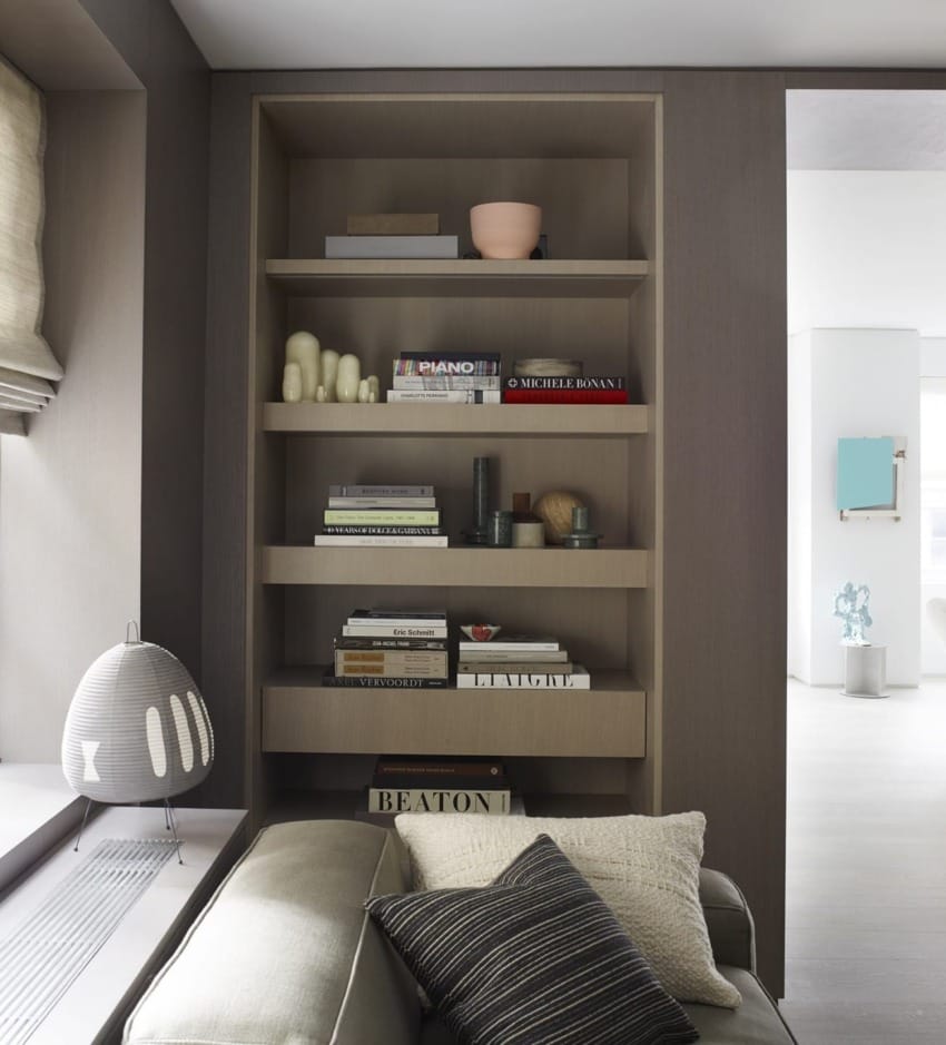 Modern living room with a built-in wooden bookshelf, decorative items, and a gray sofa with patterned cushions.