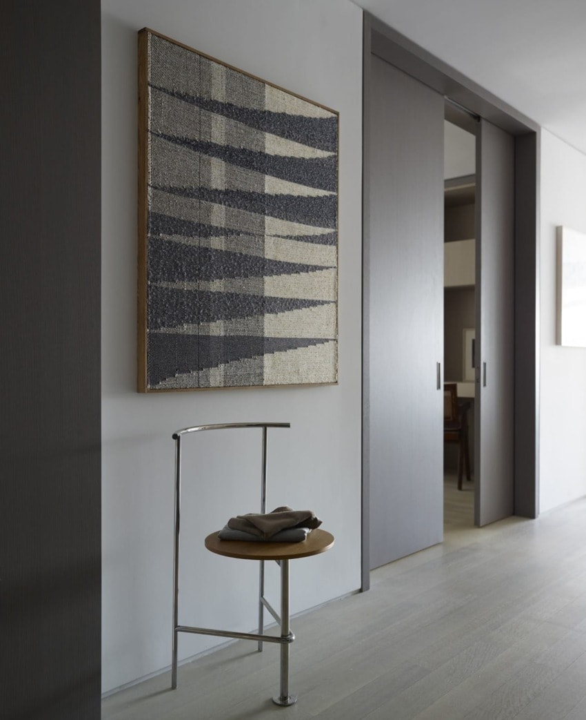 Modern hallway with abstract wall art, a sleek metal chair with wooden seat, and sliding door in a minimalist interior.