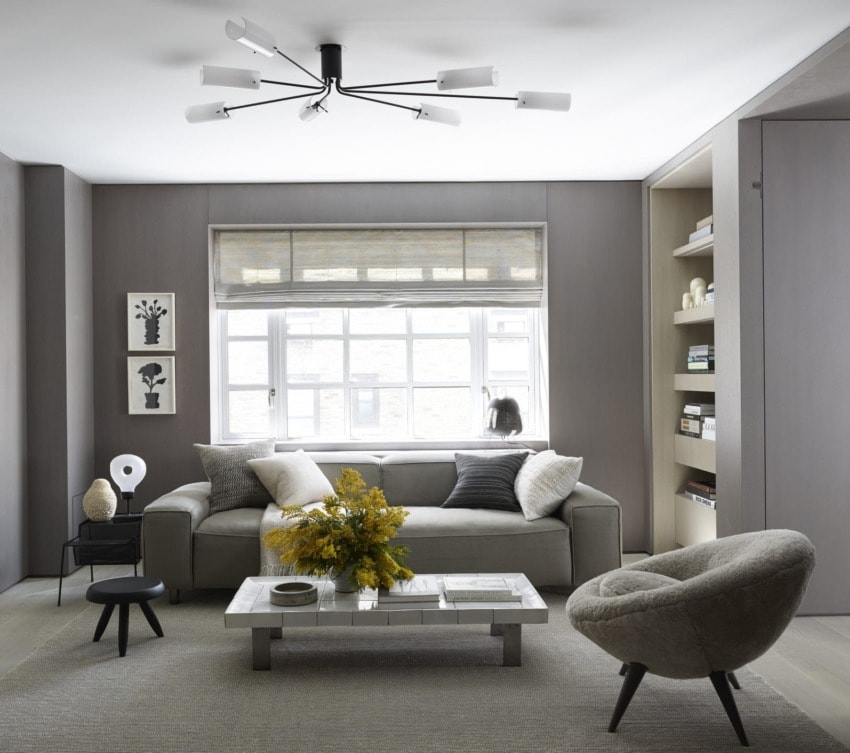 Modern living room with gray sofa, round chair, minimalist decor, large window, geometric bookshelf, and contemporary chandelier.