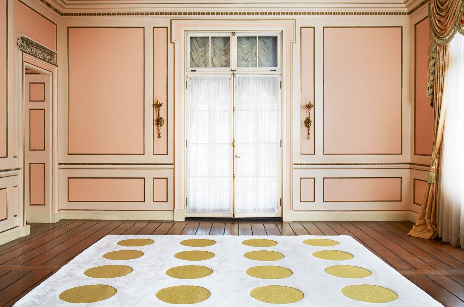 Elegant room with peach walls, gold sconces, and a patterned rug featuring large golden circles on a light background.