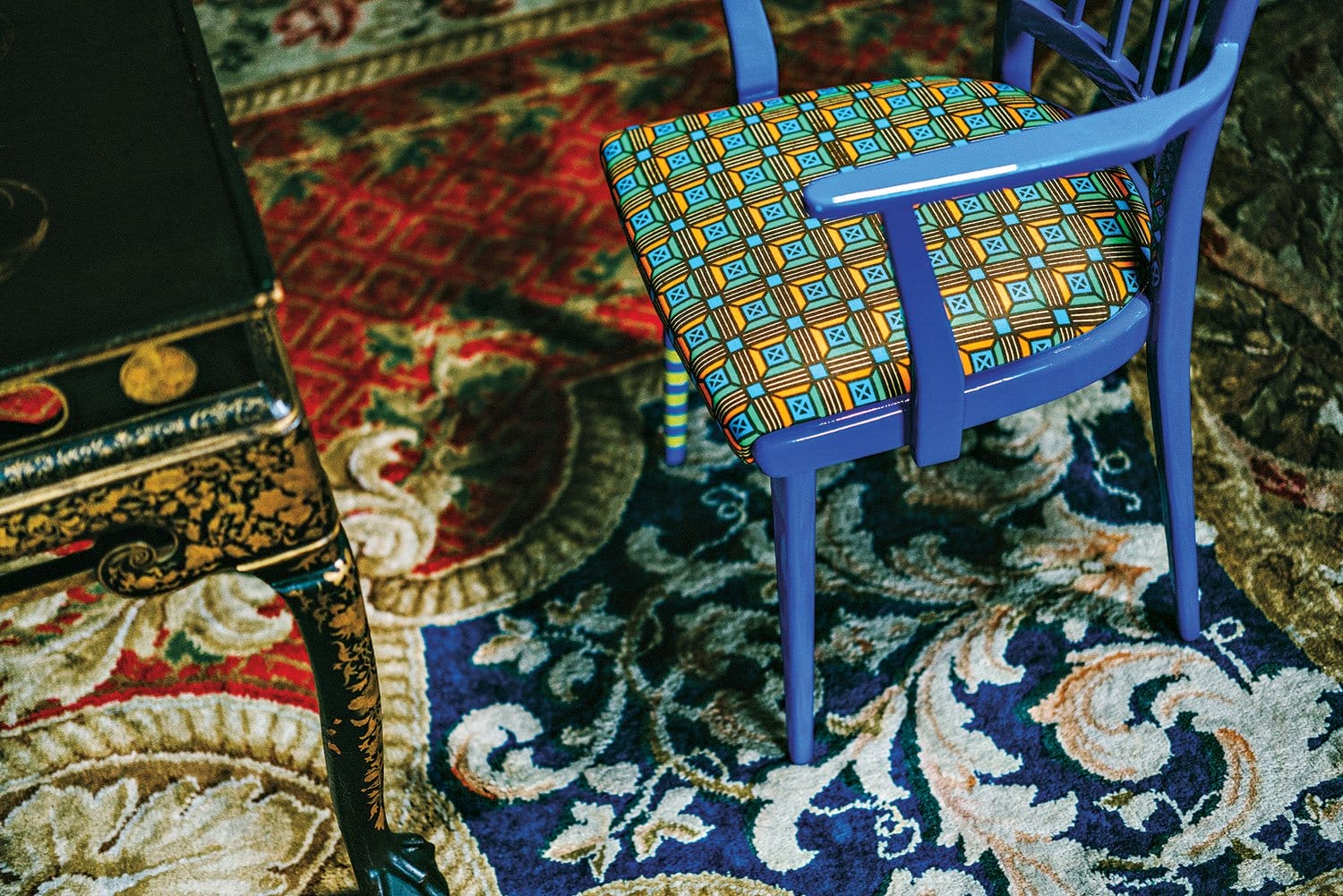 Colorful patterned chair in a room with ornate Persian rugs and dark wood table.