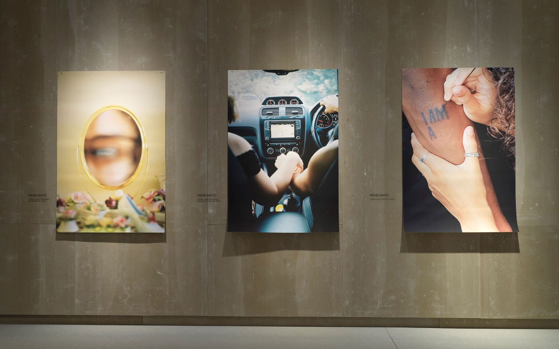 Three art pieces displayed on a wall, featuring a blurred face in a mirror, two hands in a car, and a person holding an arm.