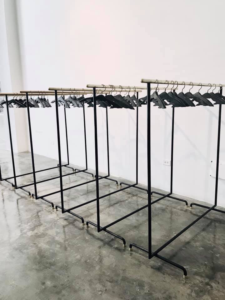 Empty clothing racks lined up against a white wall on a polished concrete floor in a minimalist room.