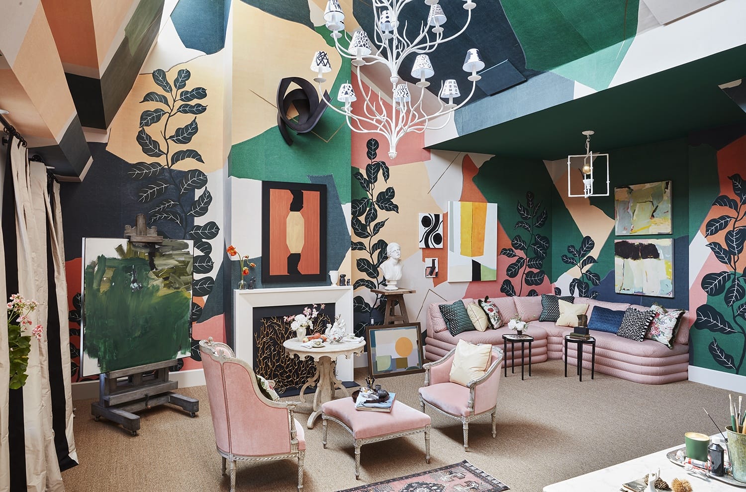 Eclectic living room with colorful abstract wall art, pink chairs, a chandelier, and a fireplace adorned with sculptures.