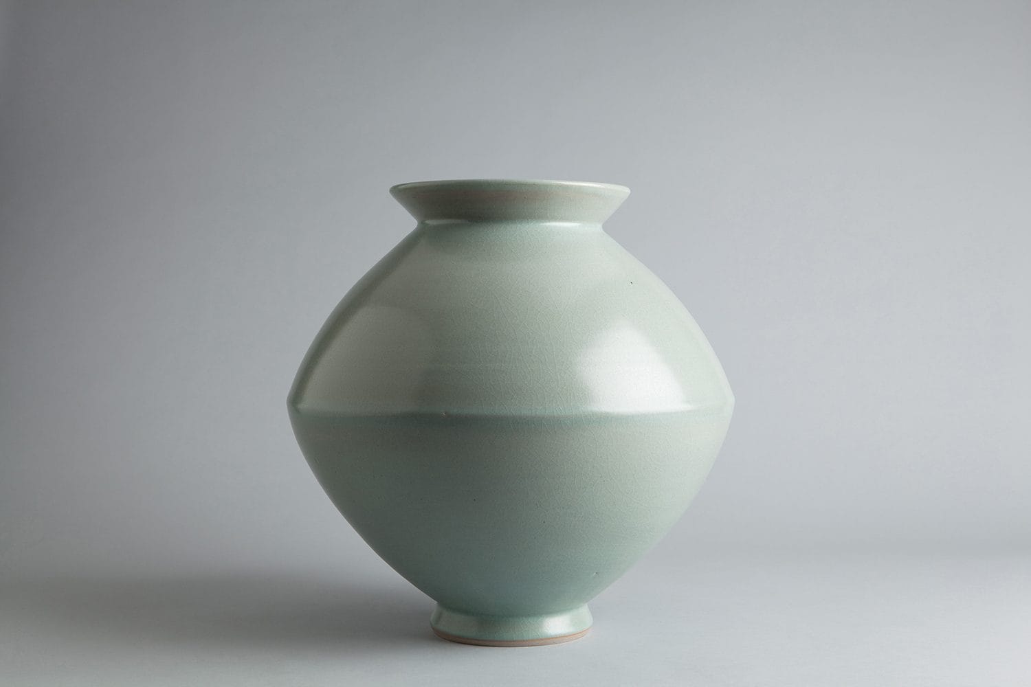 Celadon ceramic vase with a smooth, rounded design against a soft gray background.
